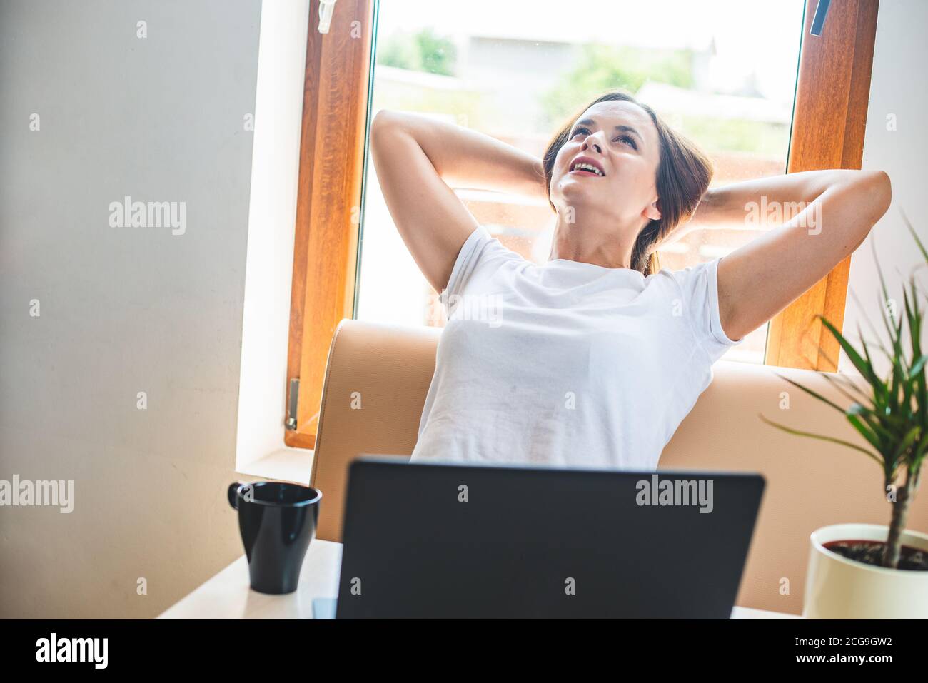 Calm smilin woman relaxing with  hands behind head, happy woman resting  satisfied after work done, enjoying break with eyes closed, peace of mind, no Stock Photo