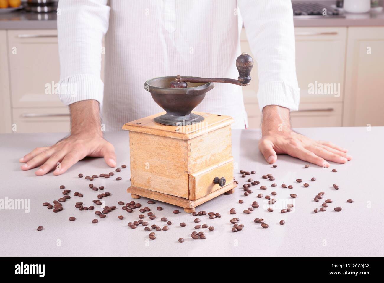 Old antique coffee grinder with coffee beans around and a man behind Stock Photo