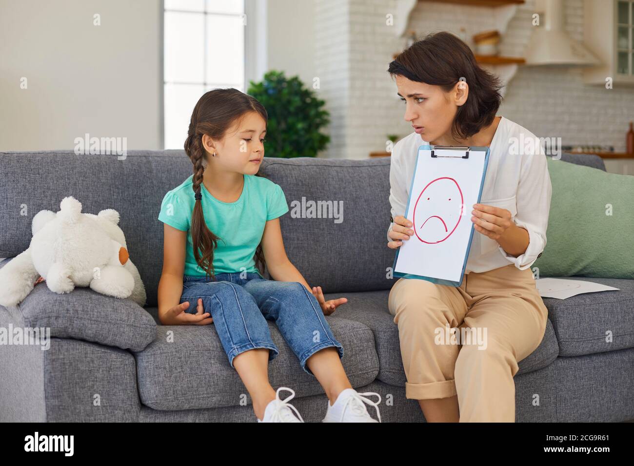 Private child psychologist having therapy session with frustrated little kid at home Stock Photo