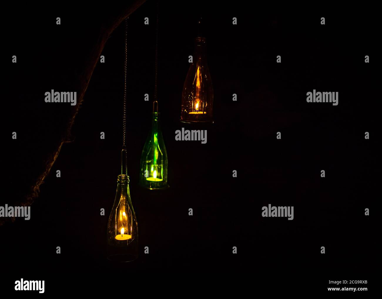 three tea light candles in glass bottles hanging from a tree branch