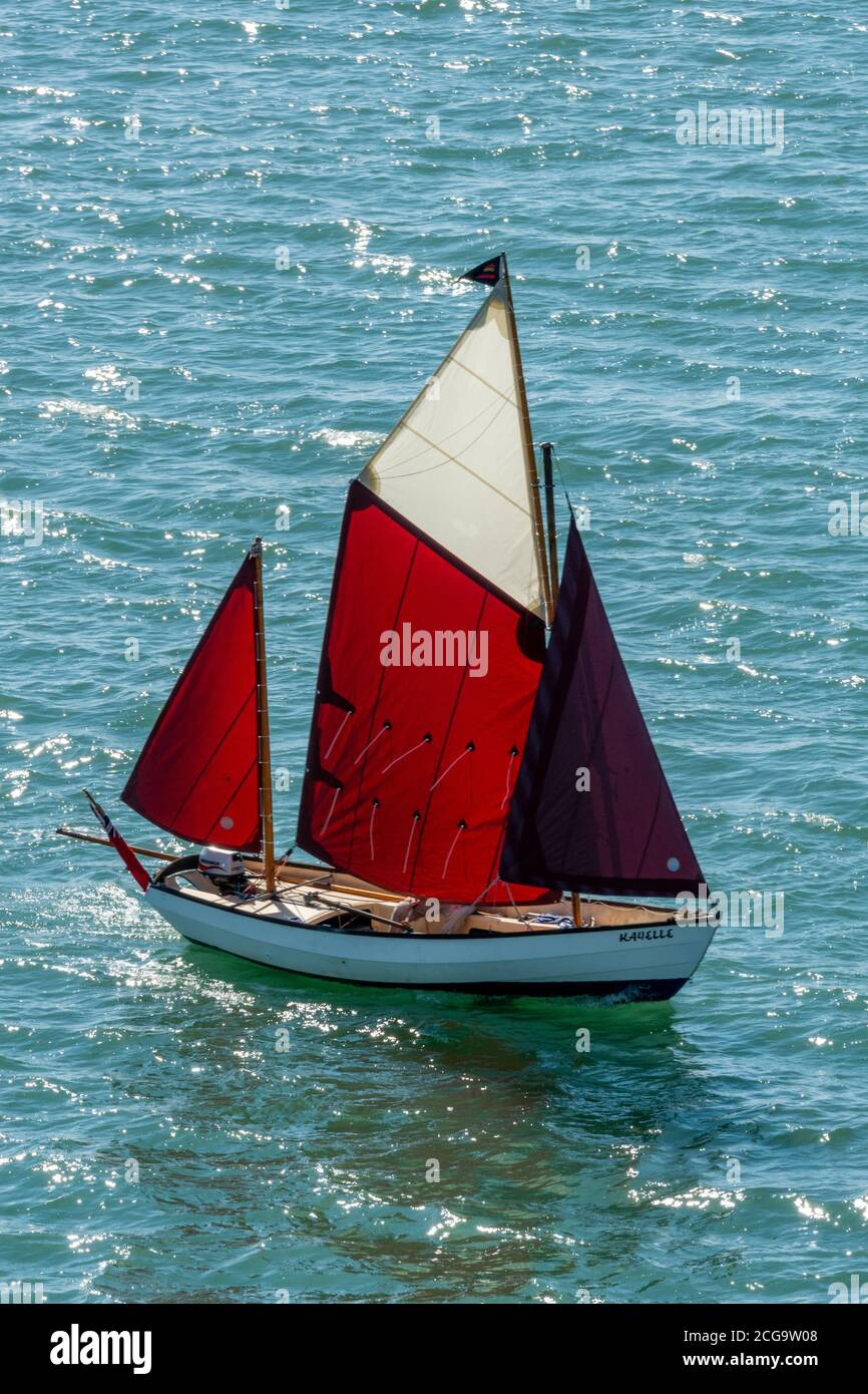 a small single manned sailing yacht under full sail with a gaff rigged