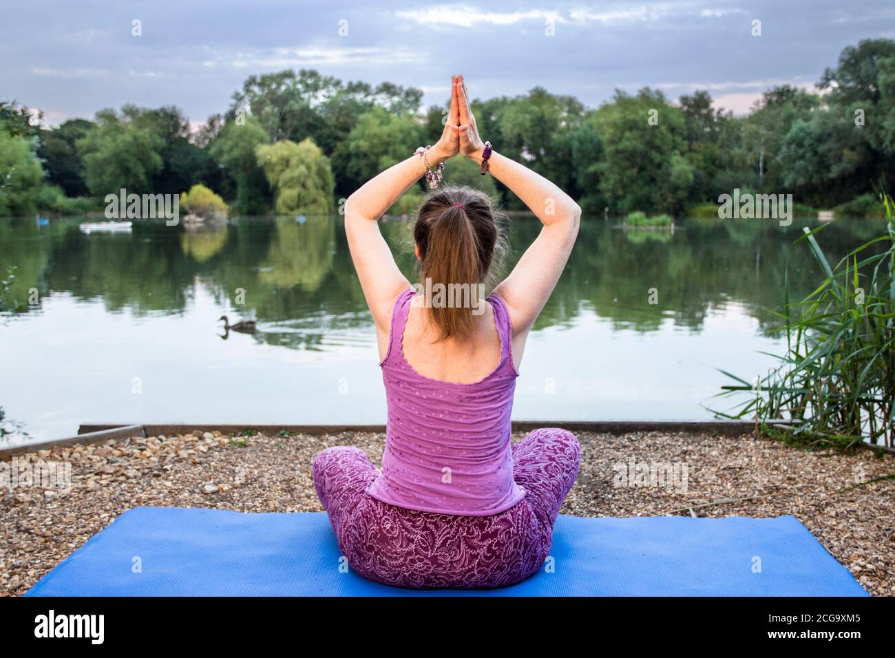 A mature yoga teacher is meditating and relaxing beside a tranquil lake by doing a yoga pose Stock Photo