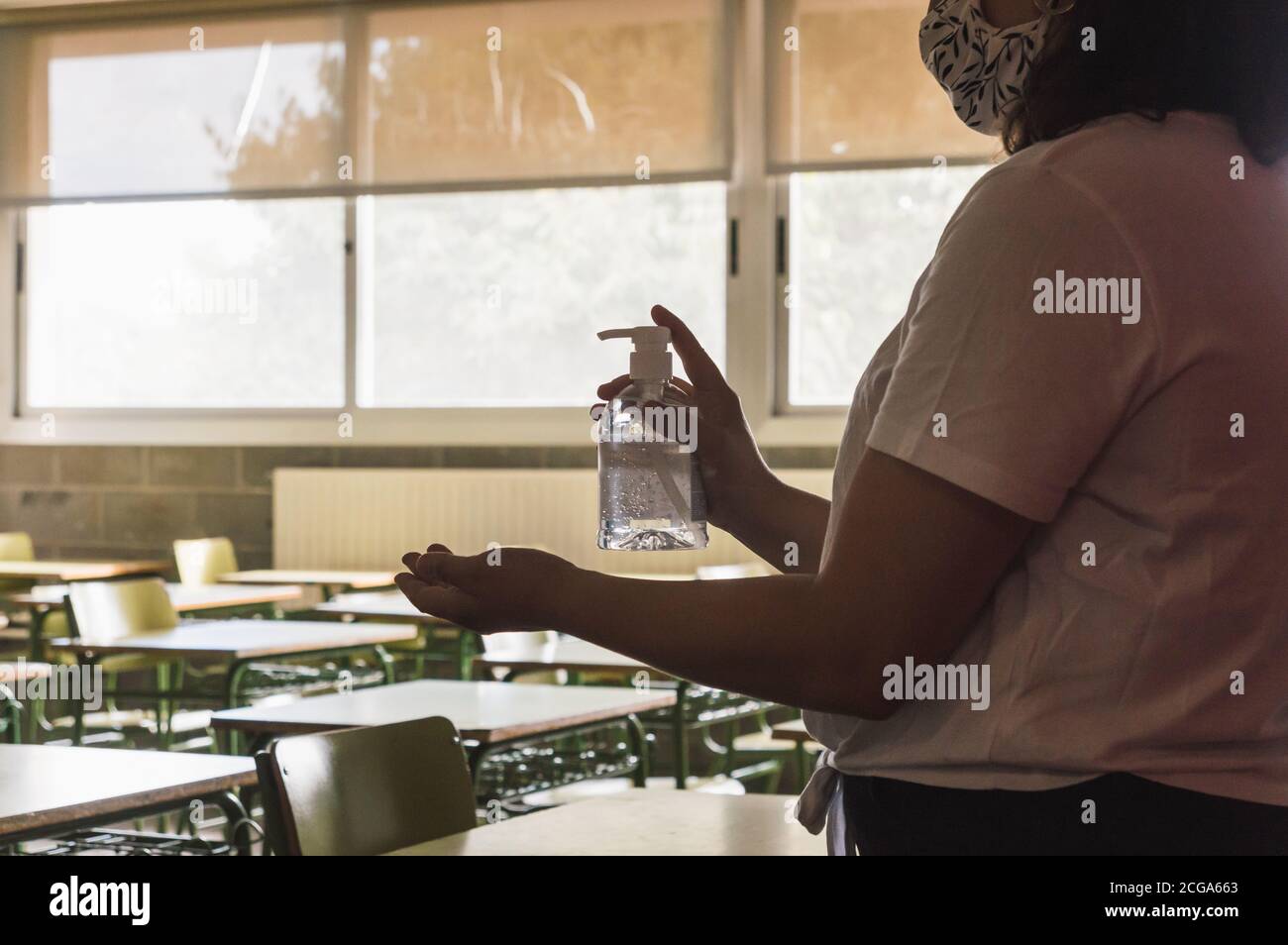 teacher wearing a face mask disinfects her hands while waiting for her students to teach Stock Photo
