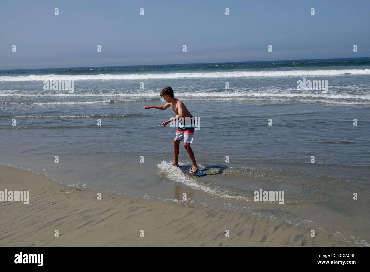 A teenage boy goes skim boarding on the waves closest to the beach shoreline. Stock Photo
