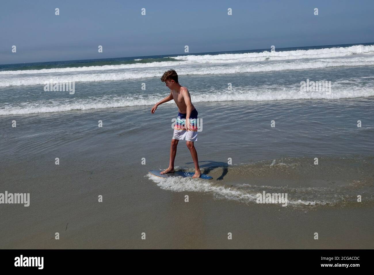 A teenage boy goes skim boarding on the waves closest to the beach shoreline. Stock Photo