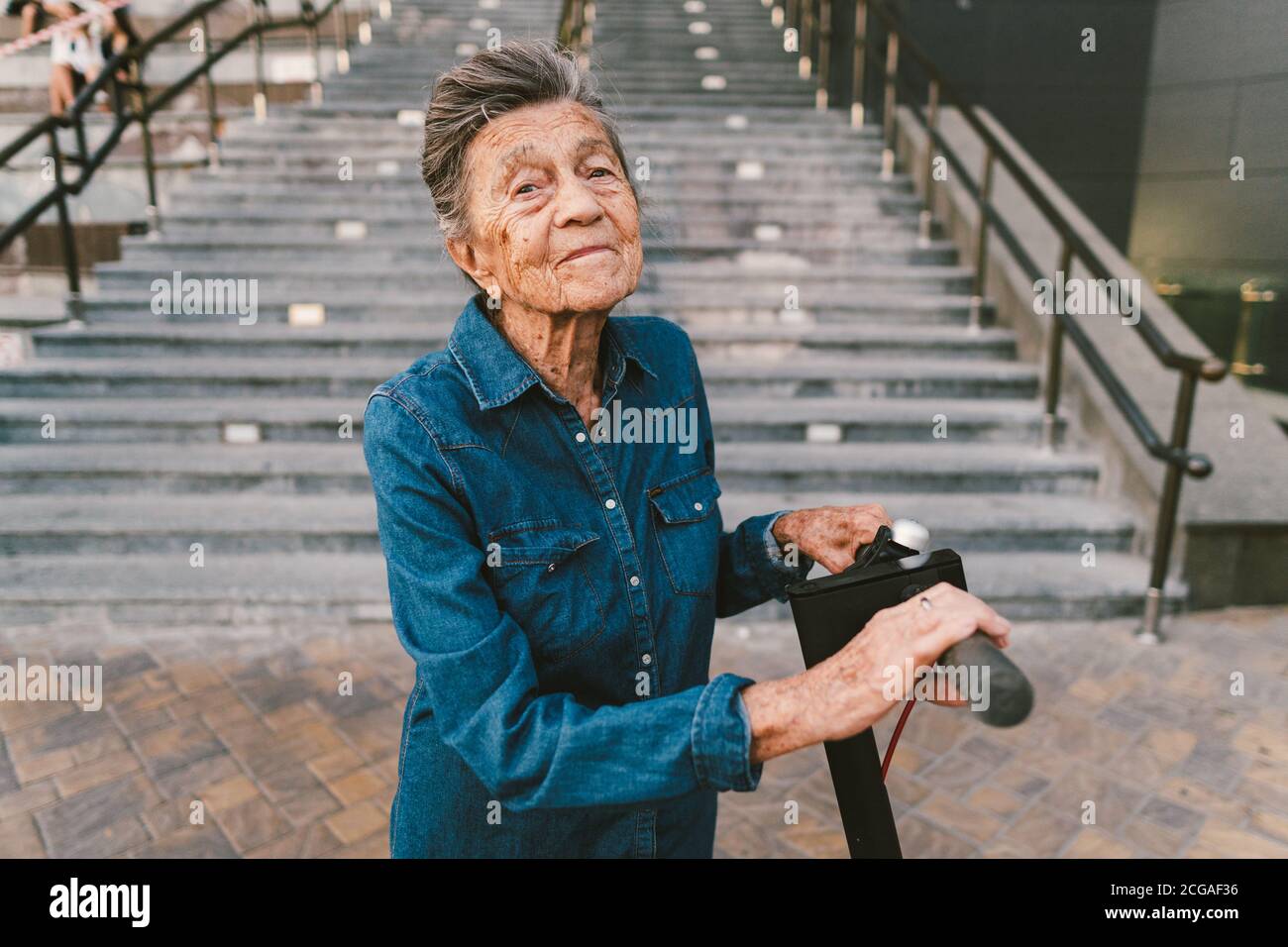 90 year old woman with gray hair, wrinkles, progressive and active uses modern electric transport scooter. Lady pensioner use eco friendly city Stock Photo