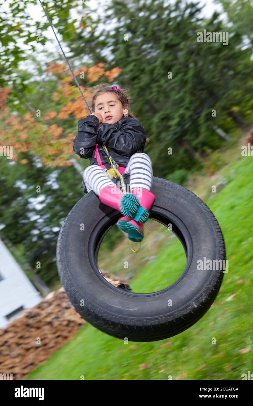 Spanish girl holds the rope attached to a tire and swings Stock Photo