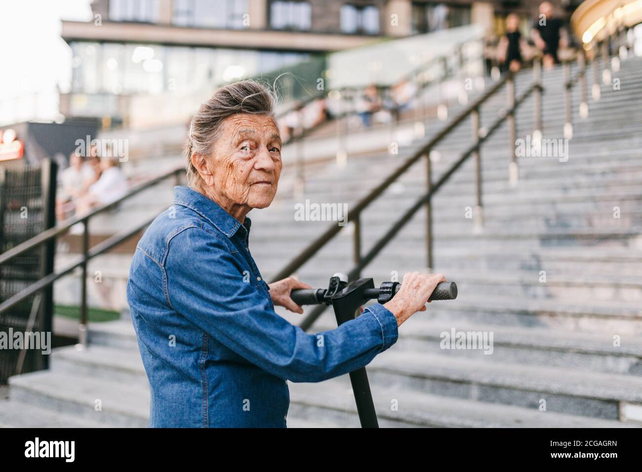 90 year old woman with gray hair, wrinkles, progressive and active uses modern electric transport scooter. Lady pensioner use eco friendly city Stock Photo