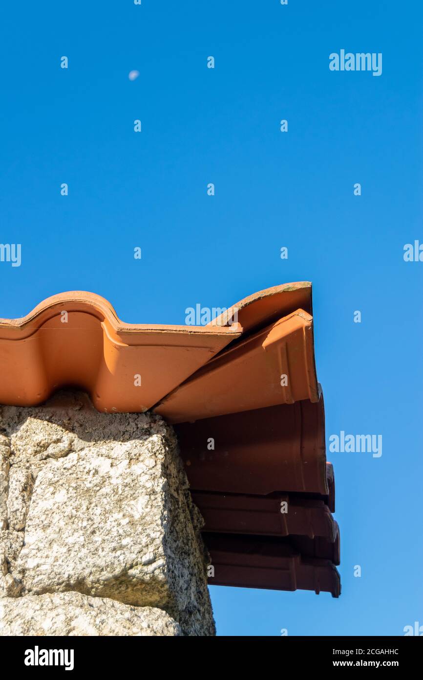 Portuguese Stone house roof corner with orange ceramics and the moon in background at day time Stock Photo