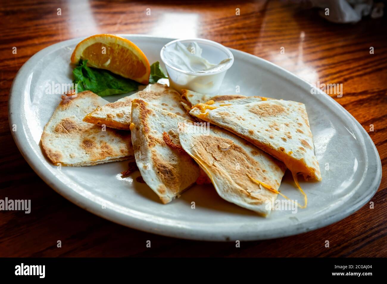 A traditional Mexican quesadilla sits on a plate with sour cream. Stock Photo