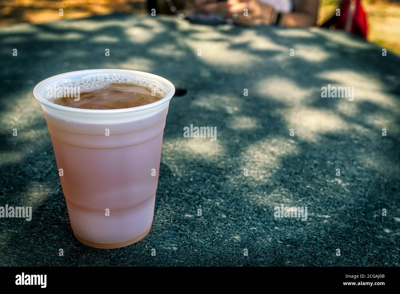 A cold cup of beer sits on a tabletop in the shade. Stock Photo