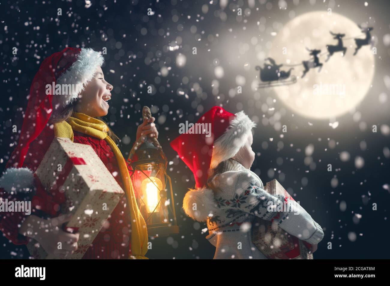 Merry Christmas and happy holidays! Cute little children with xmas presents. Santa Claus flying in his sleigh against moon sky. Kids enjoying the holi Stock Photo