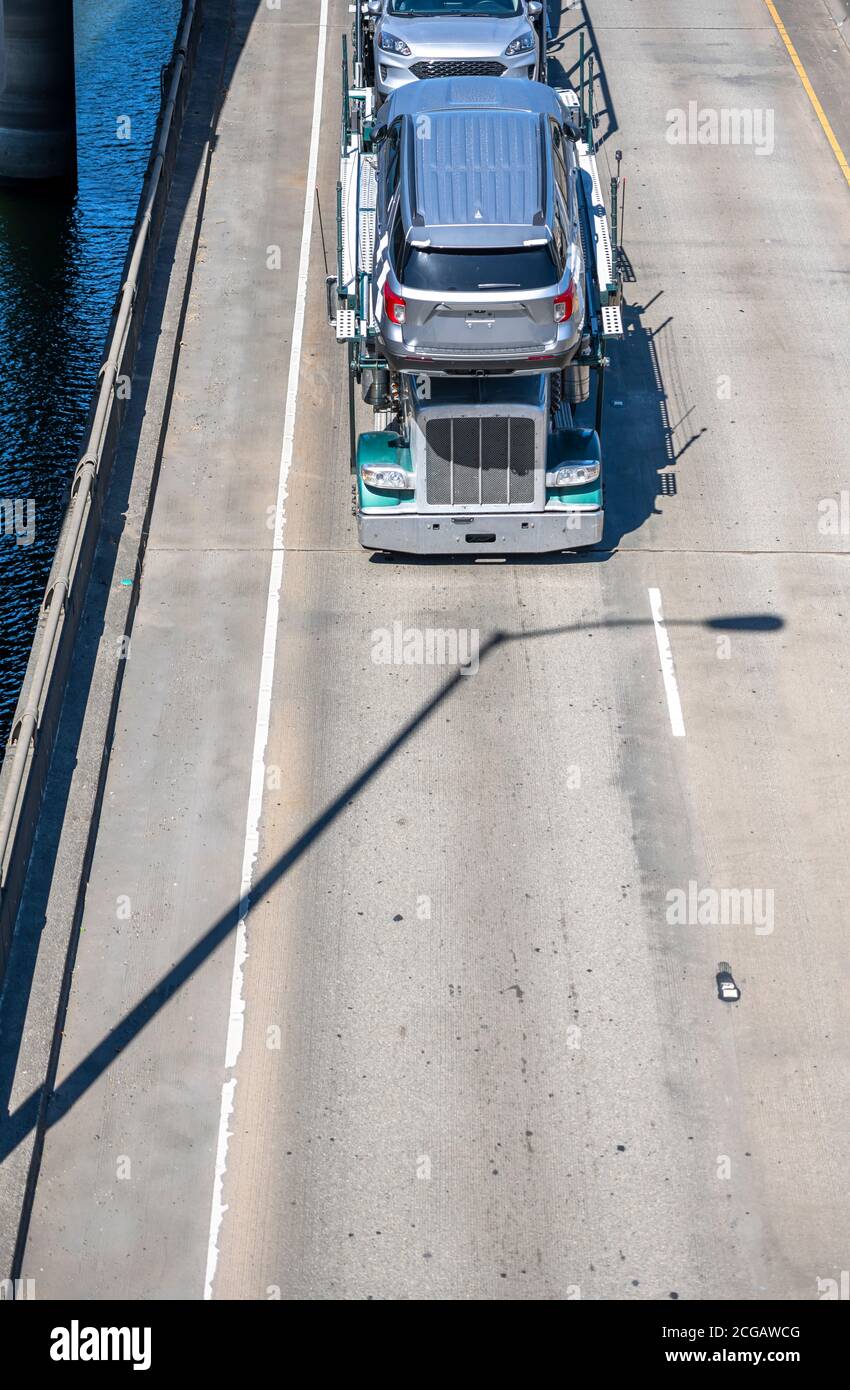 Big rig industrial professional car hauler semi truck trastor transporting cars on the two level semi trailer driving on the overpass road intersectio Stock Photo