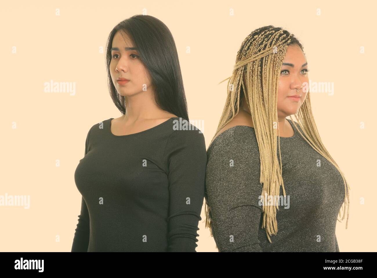 Thoughtful young Asian transgender woman and fat Asian woman looking at distance together with back to back Stock Photo