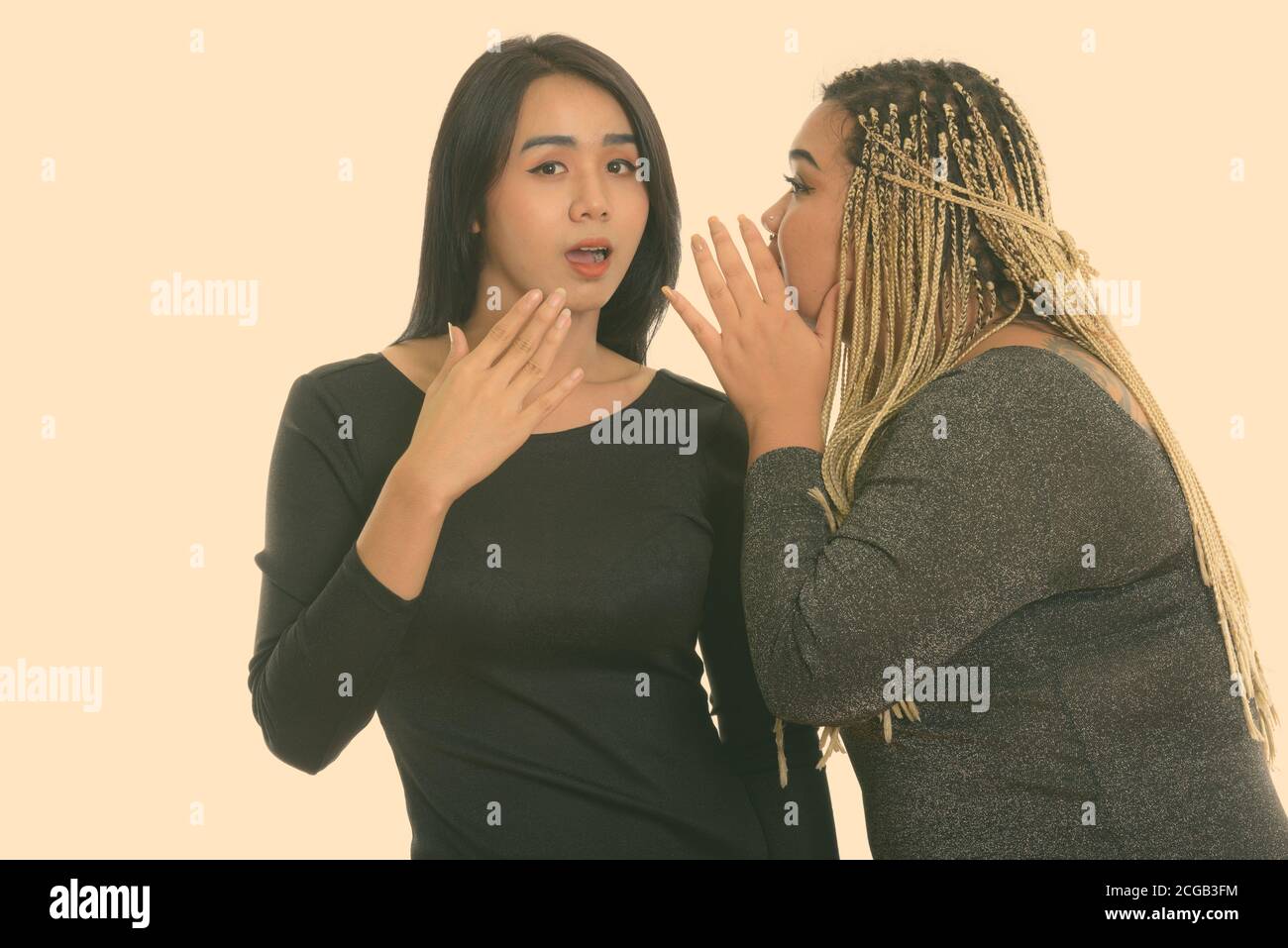 Young fat Asian woman whispering to Asian transgender woman looking shocked Stock Photo