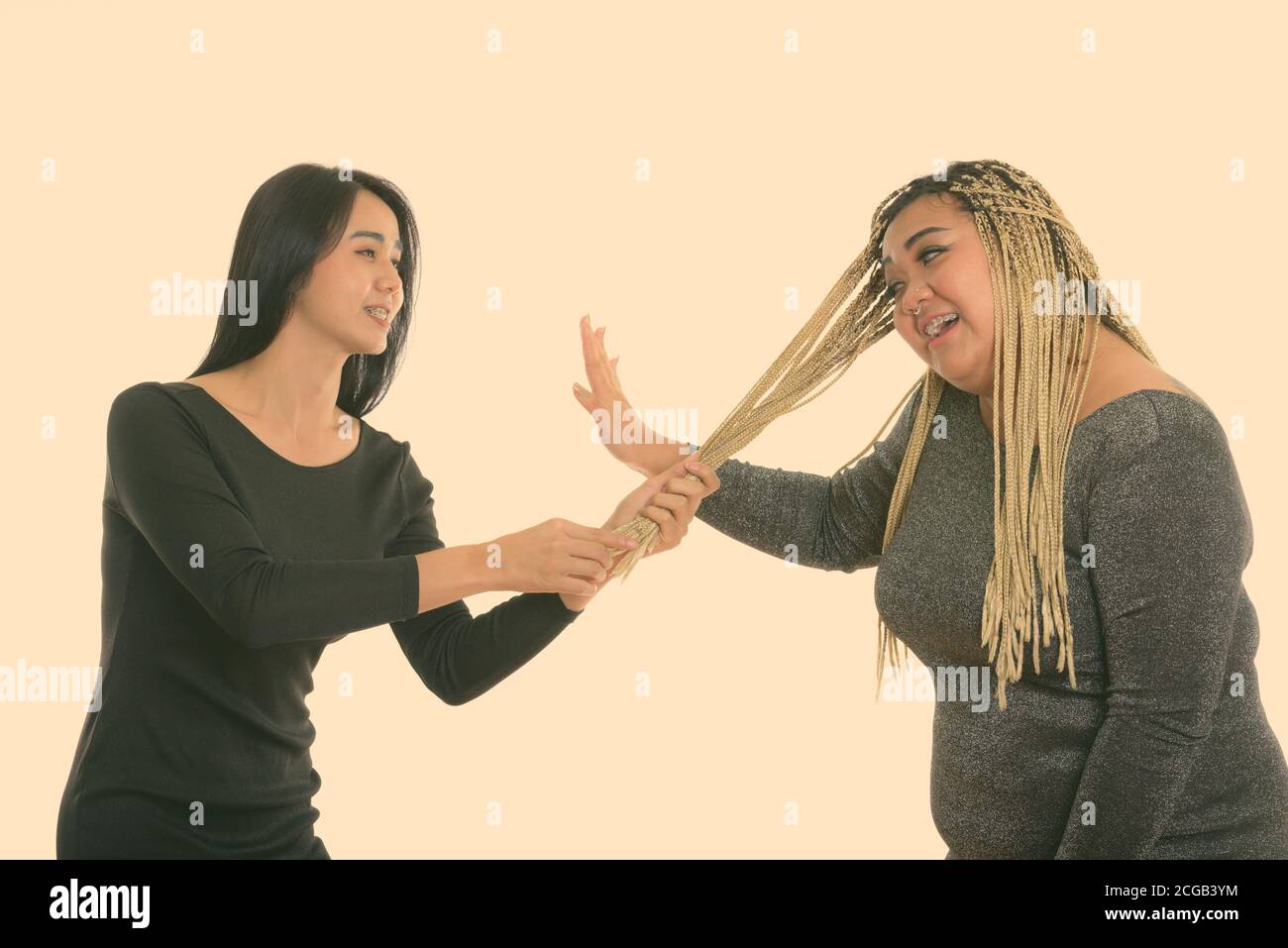Young happy Asian transgender woman smiling while pulling hair of fat Asian woman Stock Photo