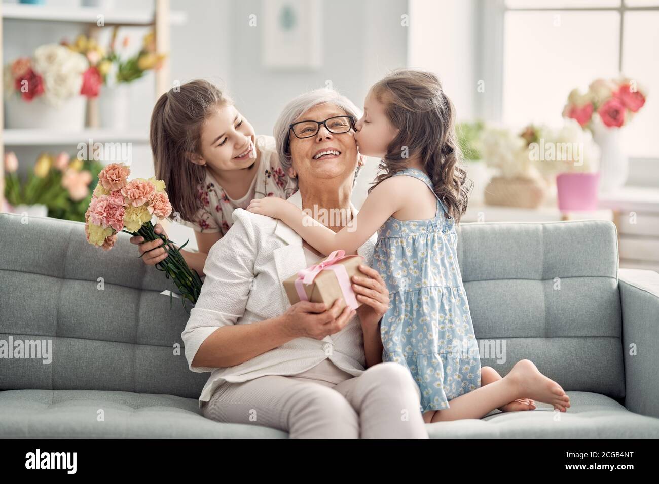 Happy mother's day! Children daughters are congratulating granny giving her flowers and gift. Grandma and girls smiling and hugging. Family holiday an Stock Photo