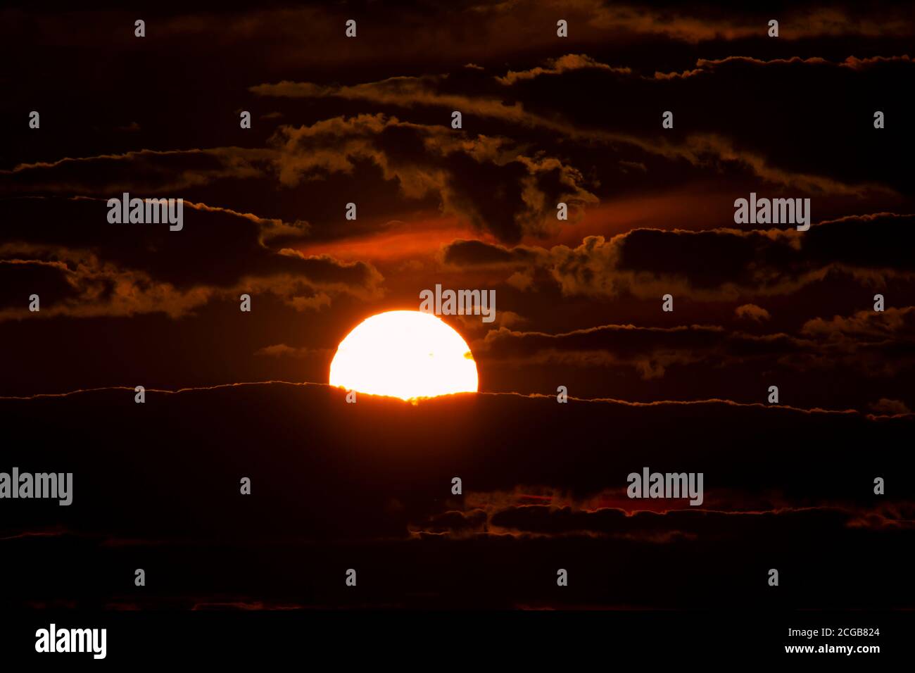 Close up image of the setting sun among the clouds. It is a low light image with sun in the middle and silhouettes of clouds surrounding it. A scenic Stock Photo
