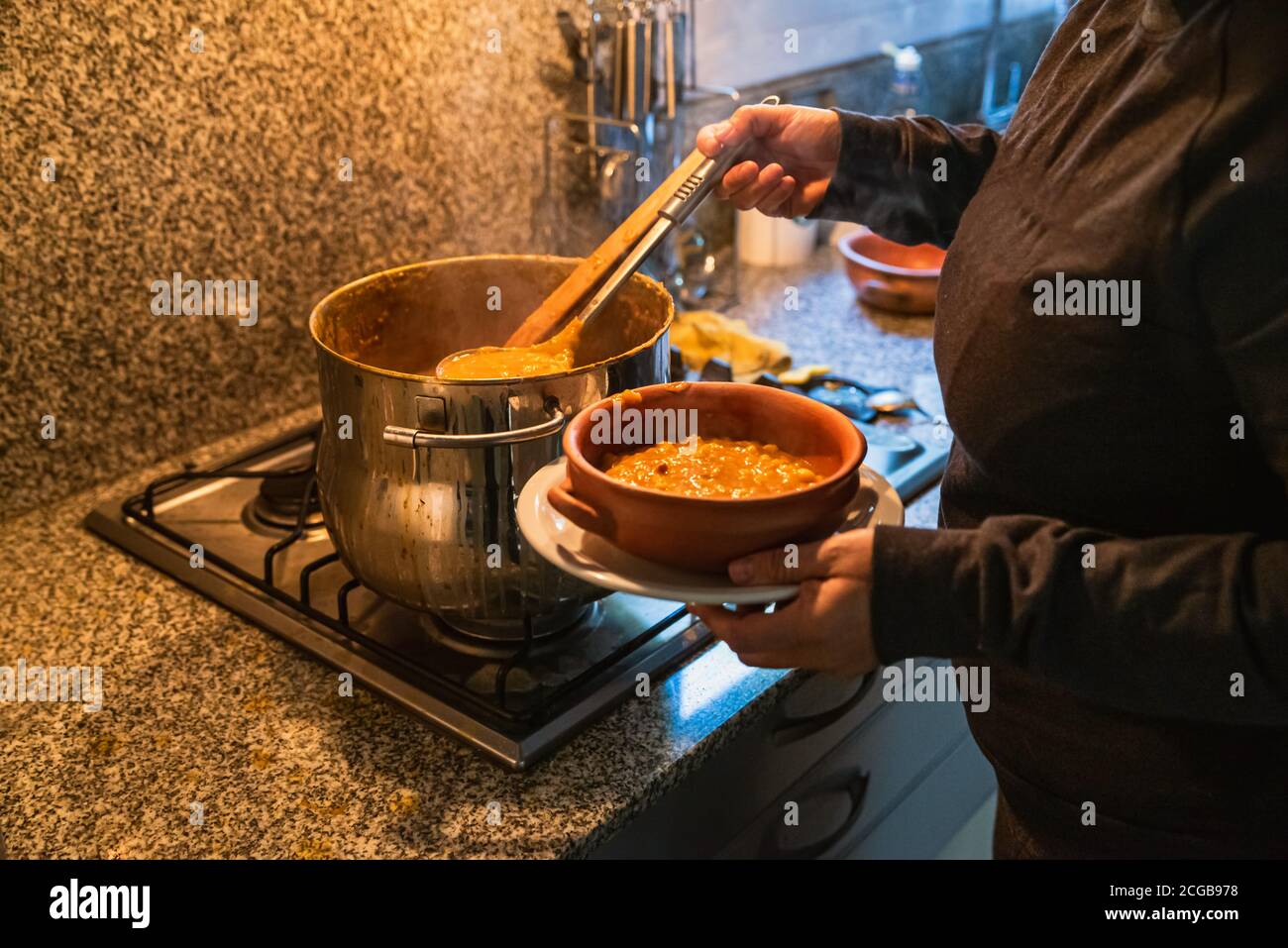 woman serving locro, typical Argentine food on handmade ceramic plates. Stock Photo