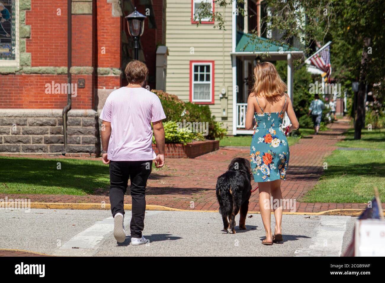 A young caucasian couple is walking in the historic district of Chestertown, Maryland with their dog. The woman has light hair color and wears floral Stock Photo