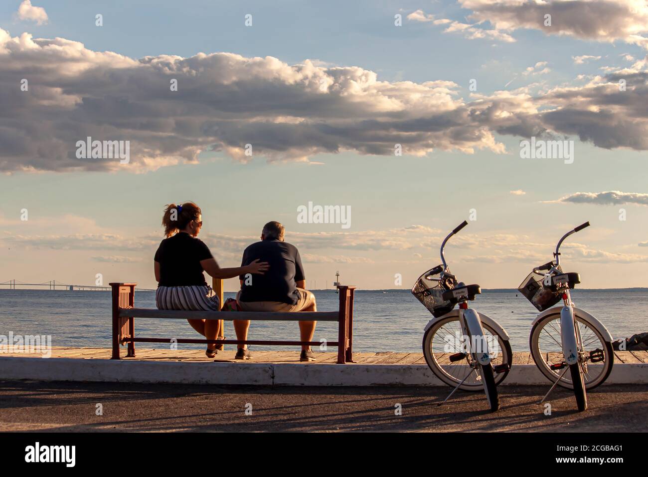 Rock Hall, MD, USA 08/30/2020: A middle aged caucasian couple is sitting on a bench by the beach. They have their identical bikes parked next to them. Stock Photo