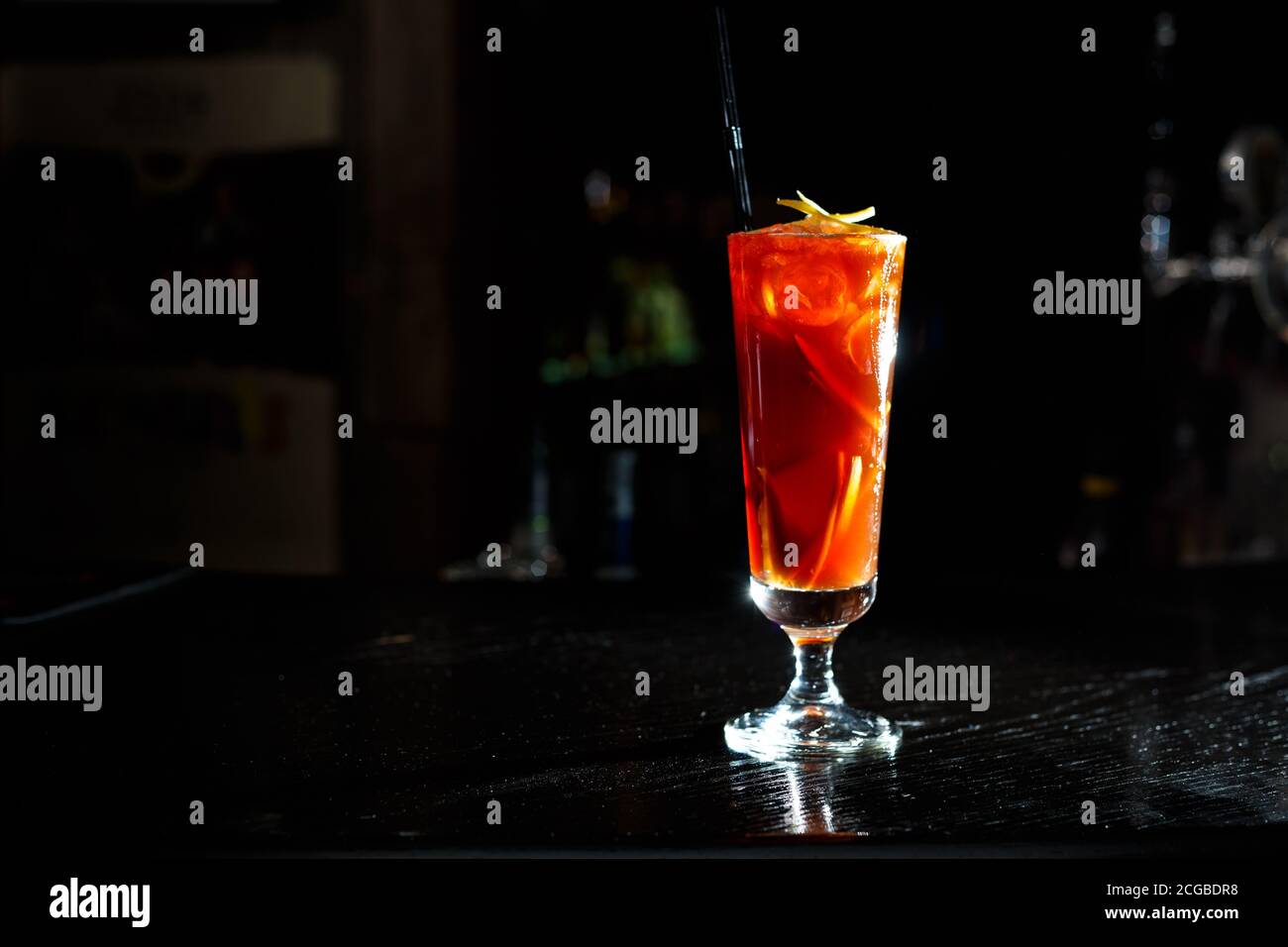A red cocktail in a tall glass stands on the counter of a dark bar. Stock Photo