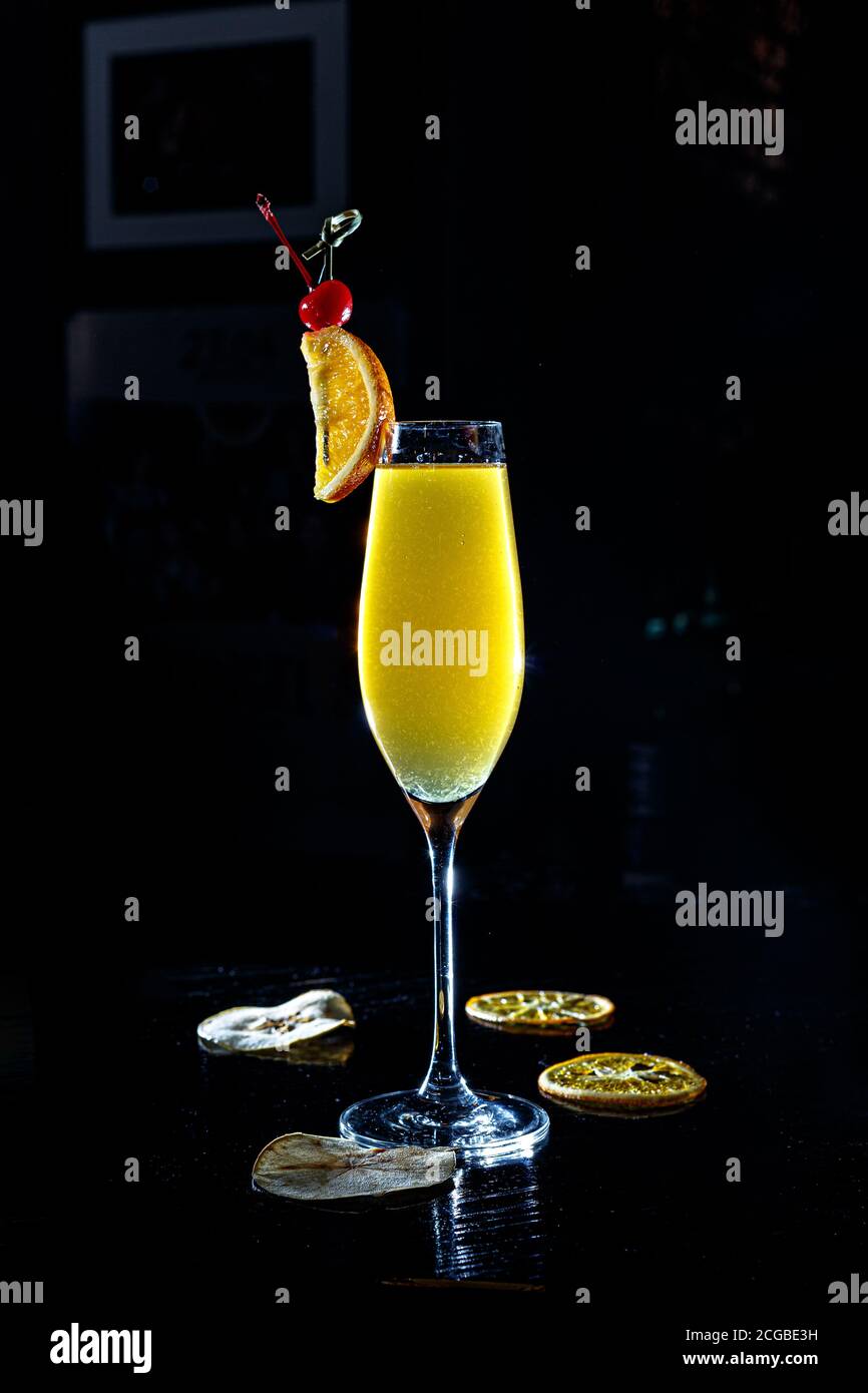 a yellow cocktail in a tall wine glass stands on the counter of a dark bar. Stock Photo