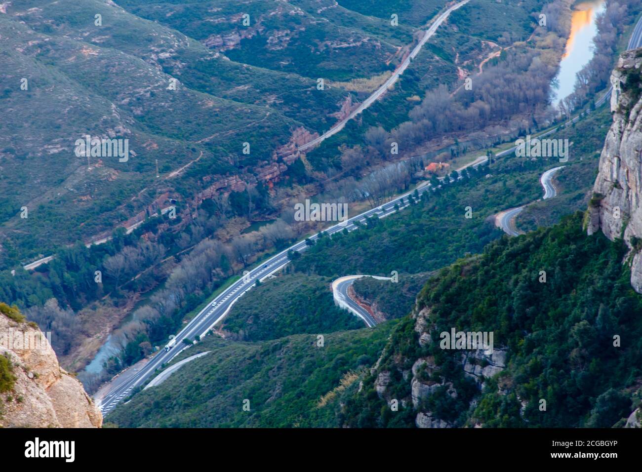 The road runs along the river between the mountains. Stock Photo