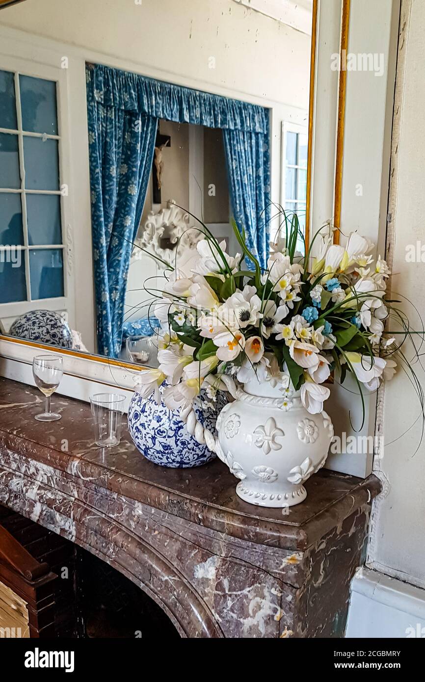 An antique vase with a bouquet of pink roses stands on the mantelpiece in the bedroom and is reflected in the mirror Stock Photo