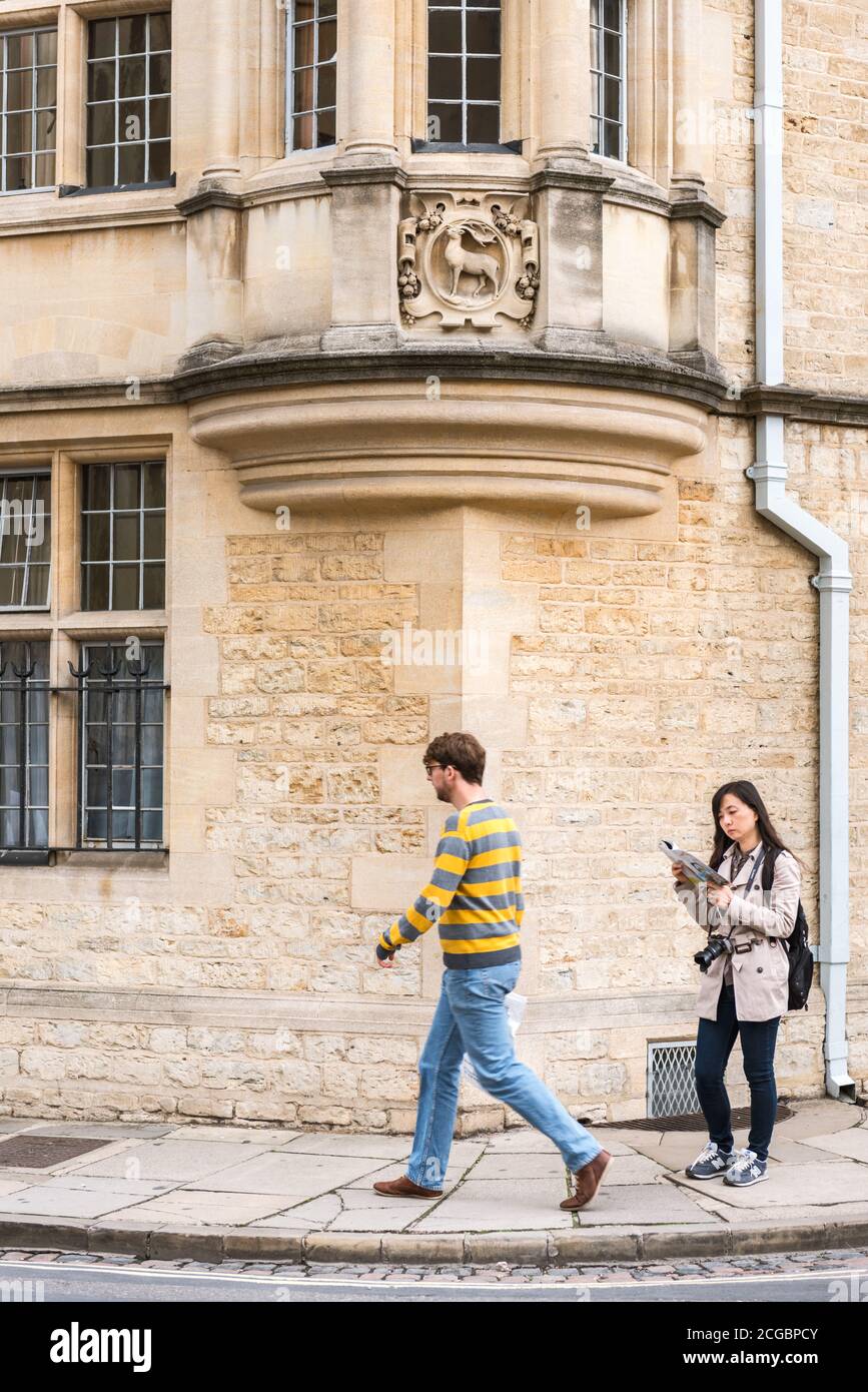 Asian woman tourist staying still reading a guide book at Catte street in Oxford Oxfordshire while local people passing by Stock Photo