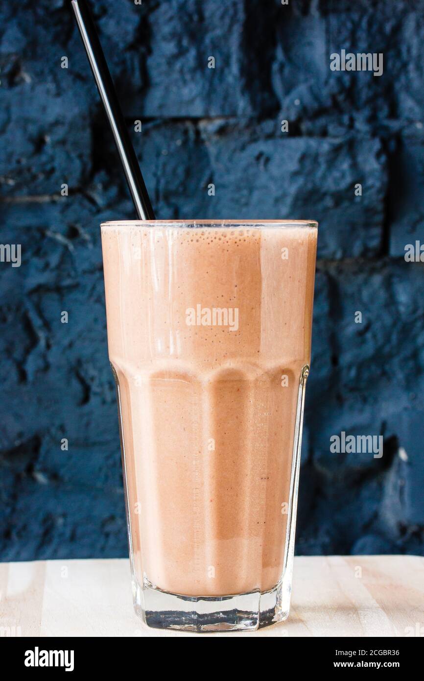 Brown Smoothie or cocktail with coffee and yogurt in a large glass glass against a dark stone wall Stock Photo