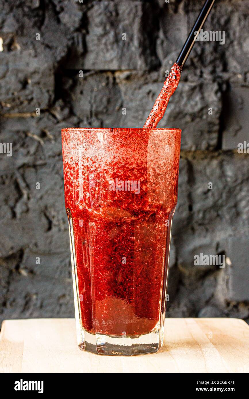 Red berry smoothie in a large glass glass against a dark stone wall Stock Photo