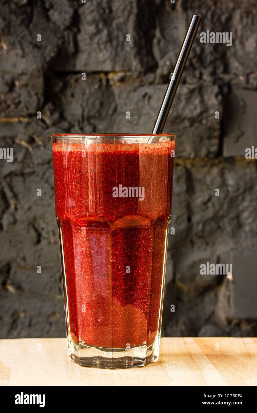 Red berry smoothie in a large glass glass against a dark stone wall Stock Photo