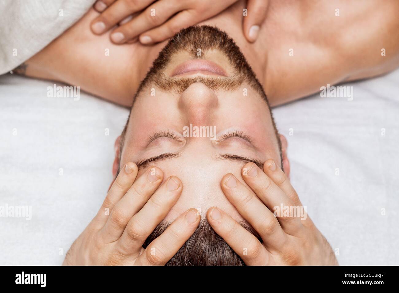 Handsome young man receiving relaxing head massage by four hand of two masseurs in health spa center Stock Photo