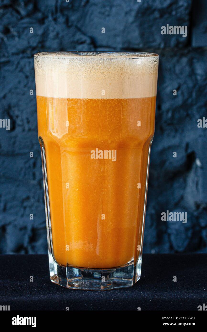 Yellow smoothie (orange, mandarin) in a large glass cup against a dark wall. Stock Photo