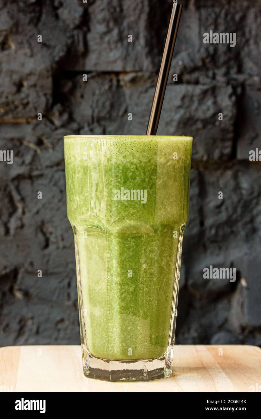 Green smoothie made from herbs and vegetables in a large glass glass against a dark stone wall Stock Photo