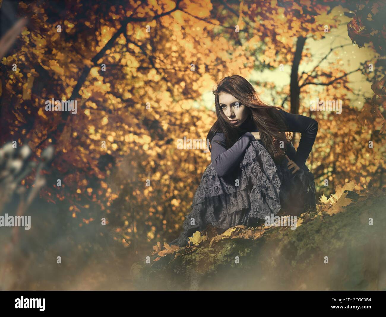 young woman in vintage dress on a forest stone at fall season sunset ...