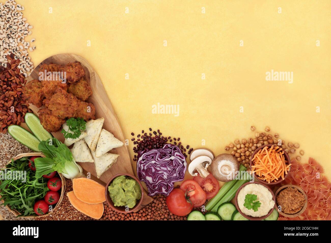 Plant based vegan food for a healthy diet with vegetables, fruit, pasta, samosas, bajis, legumes & dips. Stock Photo