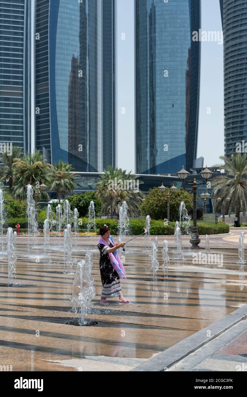 A tourist taking a selfie in the water fountain feature in front of the Etihad Towers, Abu Dhabi. Stock Photo