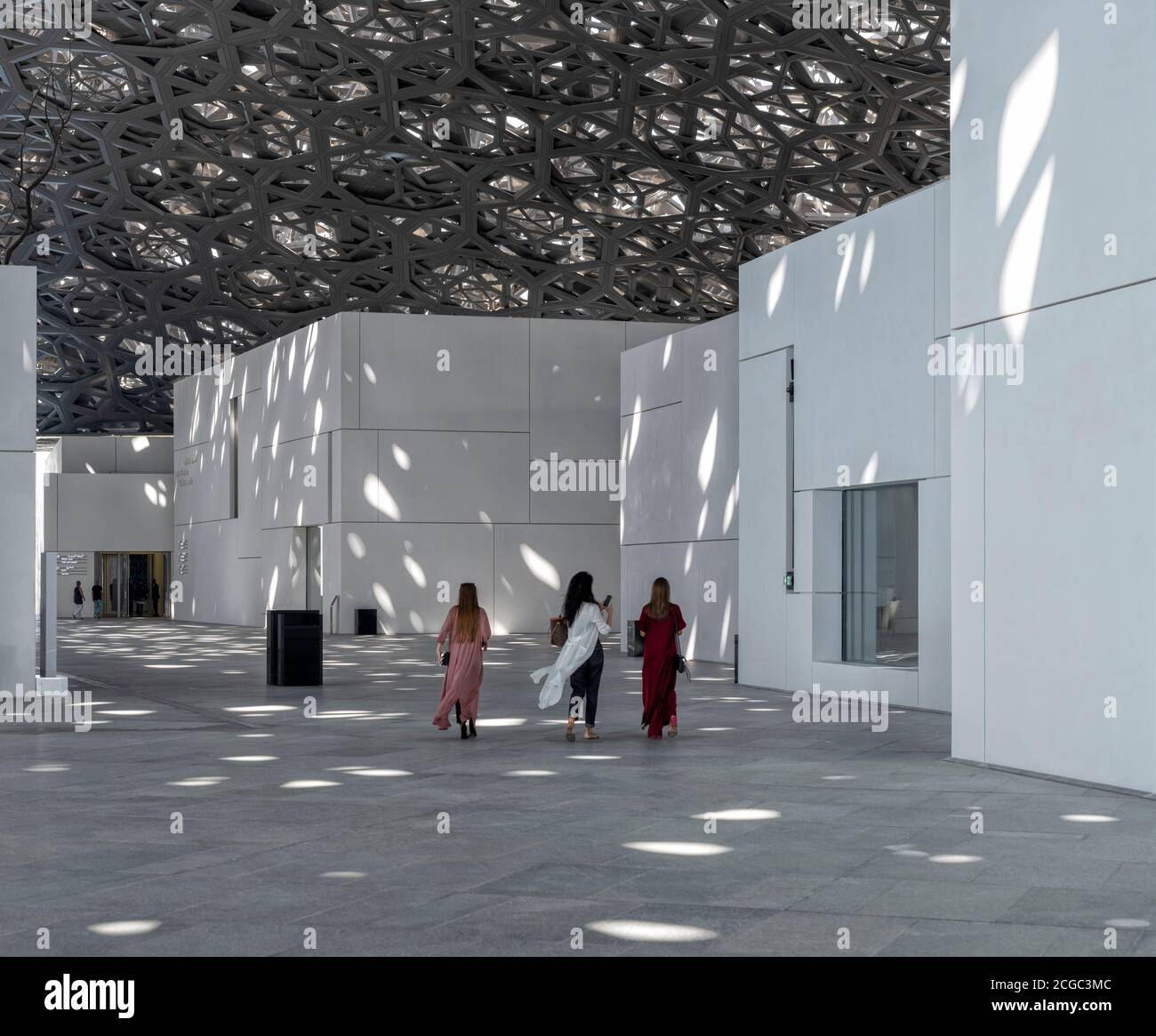 An interior shot of the Louvre Abu Dhabi which includes visitors, its overhead hi-tech roof with filtering light, and white facade walls of its various exhibiting spaces. Opened Novemeber 2017. Stock Photo