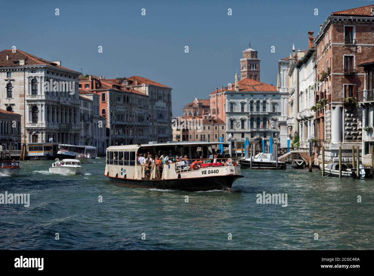 Venice's water way with local vernacular buildings peppering the water front. Shot taken from a boat, showing one of Venice's water buses and locals on their boats on the canal. Stock Photo