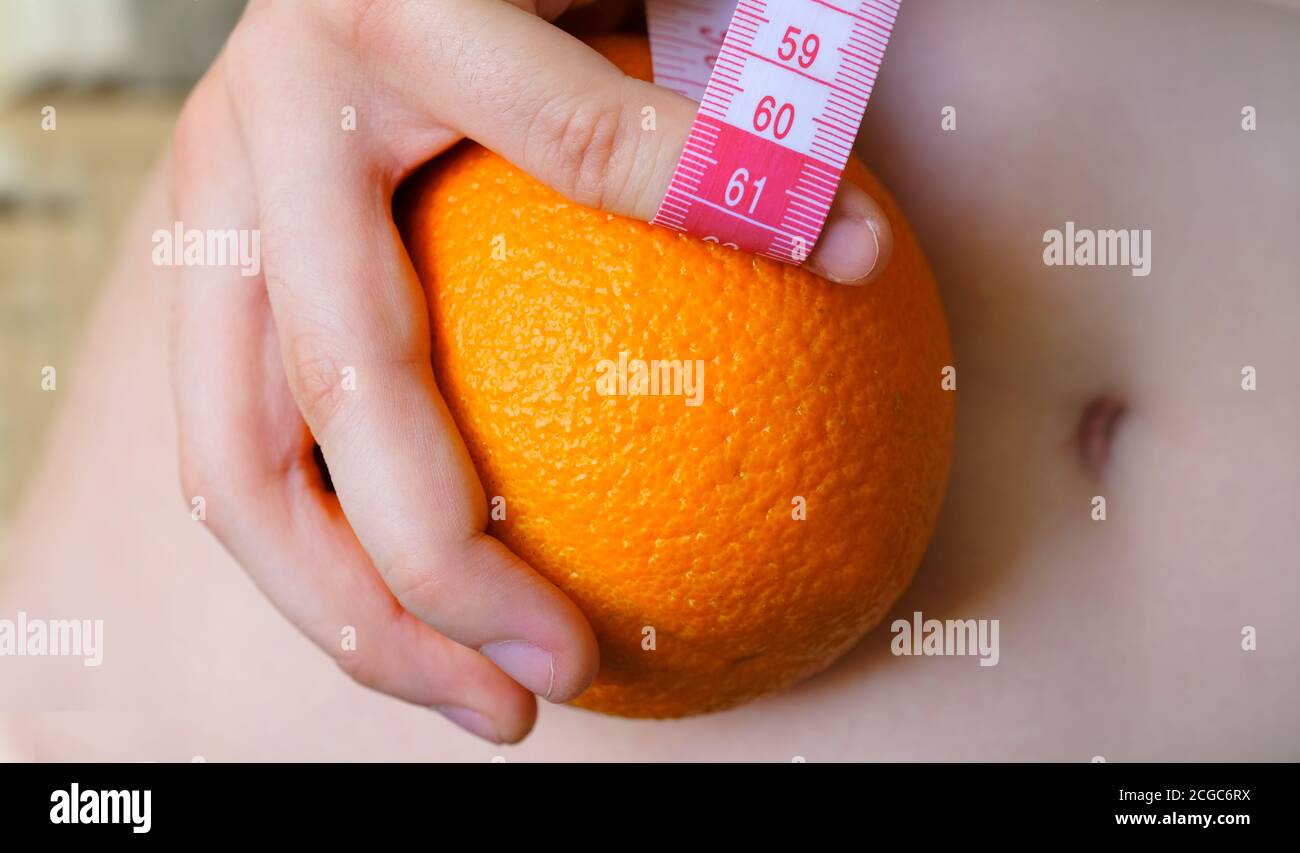 Woman is holding orange.Female body with cellulite. Tape measure. Skin care and anti cellulite massage. Stock Photo