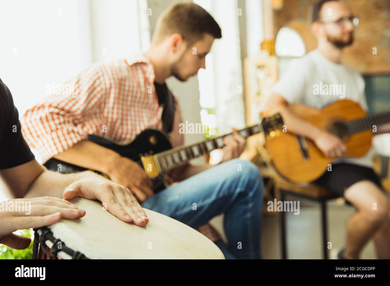 Songs. Musician band jamming together in art workplace with instruments. Caucasian men and women, musicians, playing and singing together. Concept of music, hobby, emotions, art occupation. Stock Photo