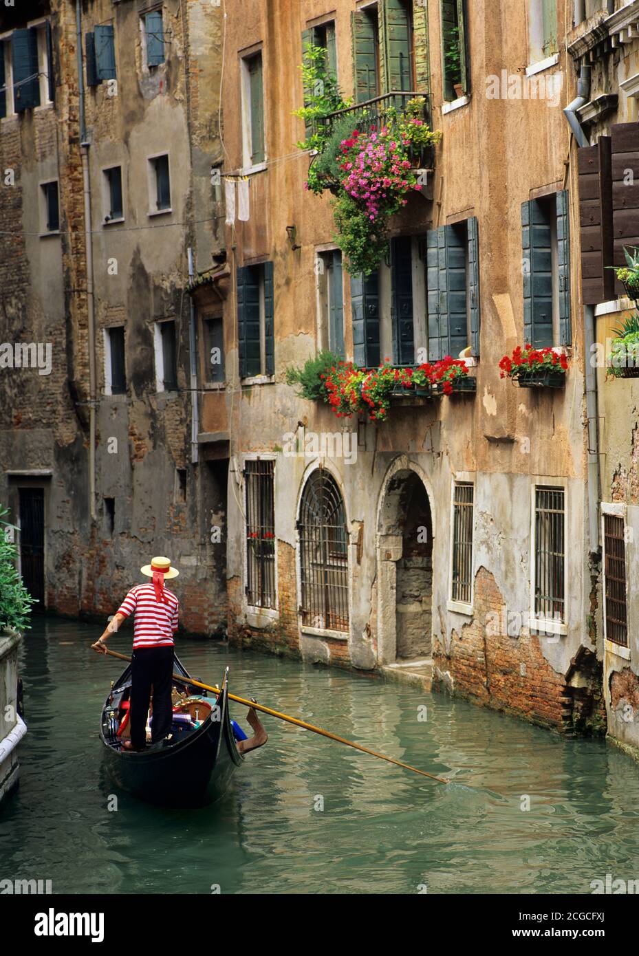 Gondola and Gondolier and flower-filled window boxes on side canal in Venice Stock Photo