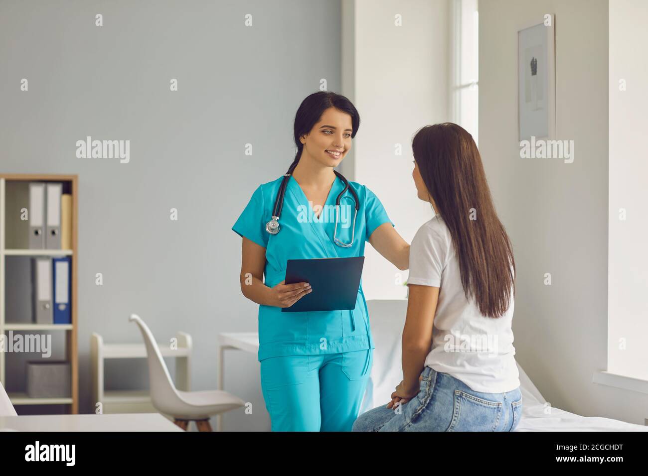 Young smiling doctor calming down sitting woman patient during consultation in medical clinic Stock Photo