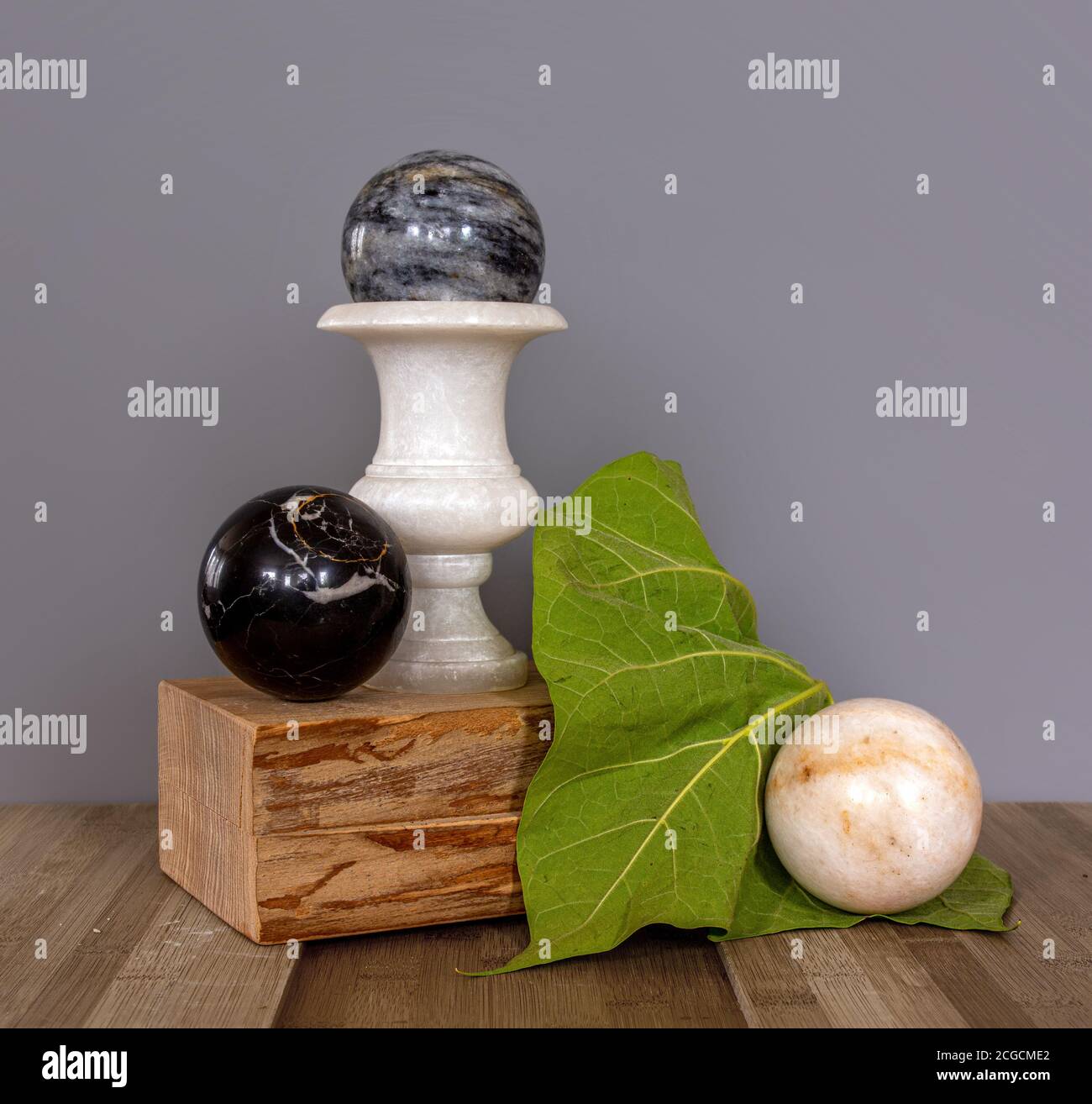 Vase and balls made of marble on a wooden stand. Large green leaf. Still life. Vintage. Stock Photo