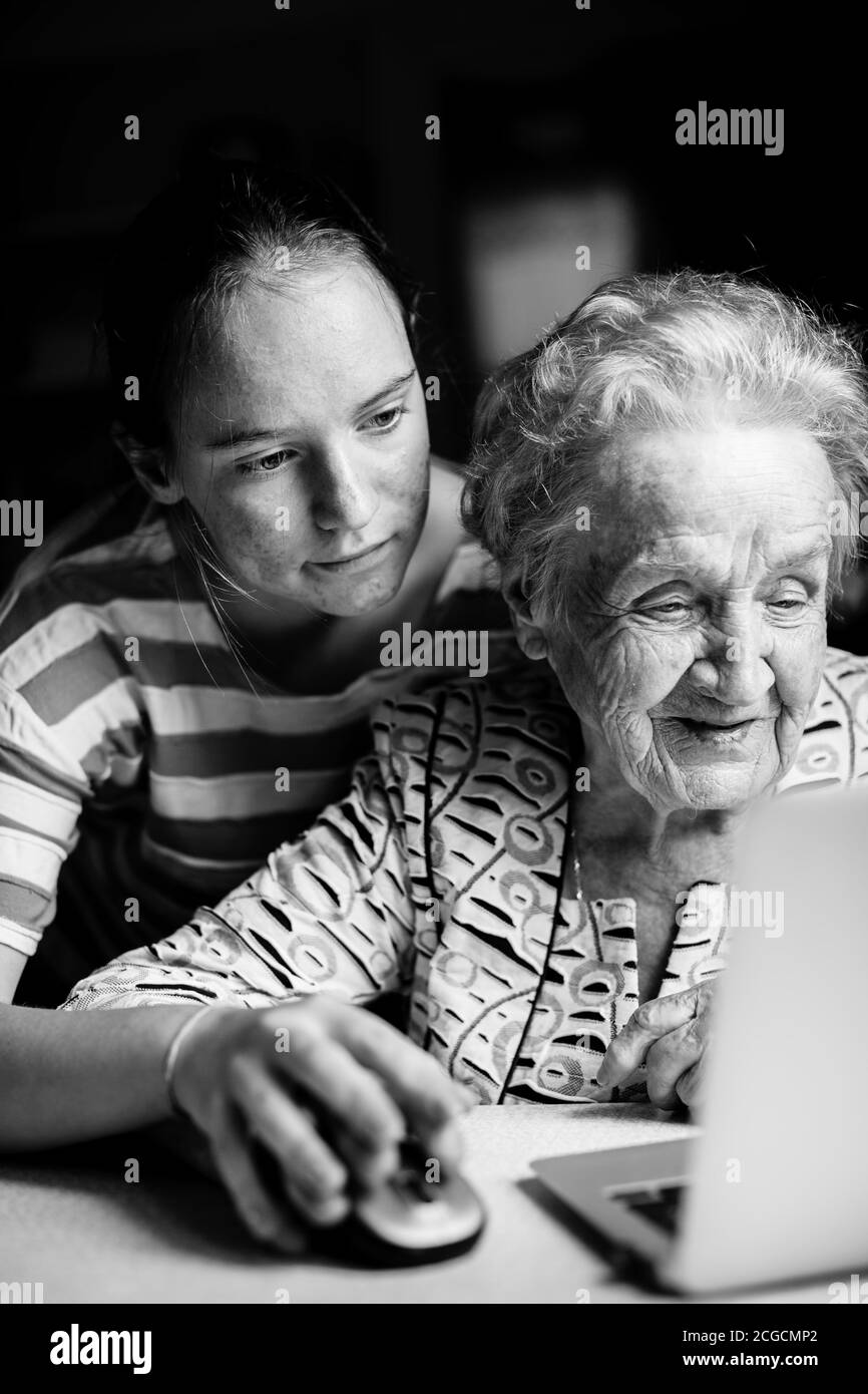 Girl teaches her grandmother to work on the computer. Black and white photo. Stock Photo
