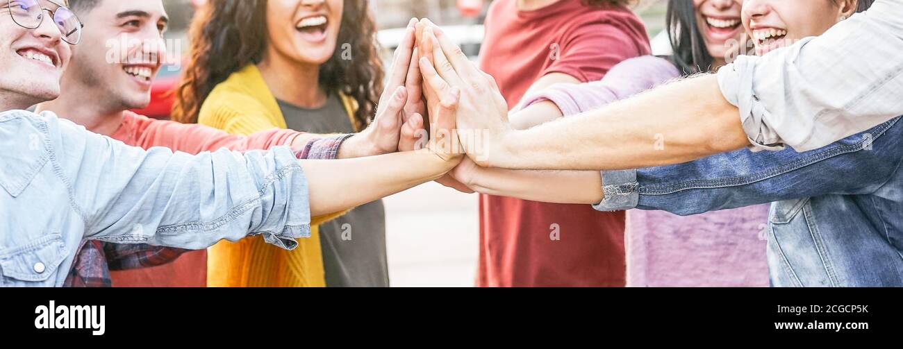 Group of diverse friends stacking hands outdoor - Happy young people having fun joining and celebrating together Stock Photo