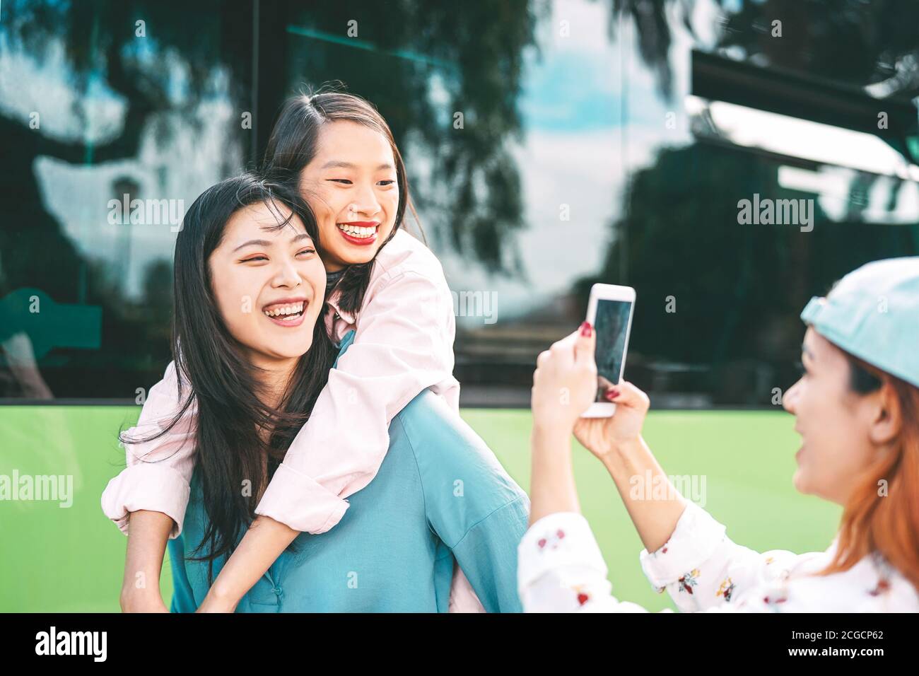 Millennial Asian girls using mobile phone outdoor - Young happy people having fun with new smartphone app technology outside Stock Photo