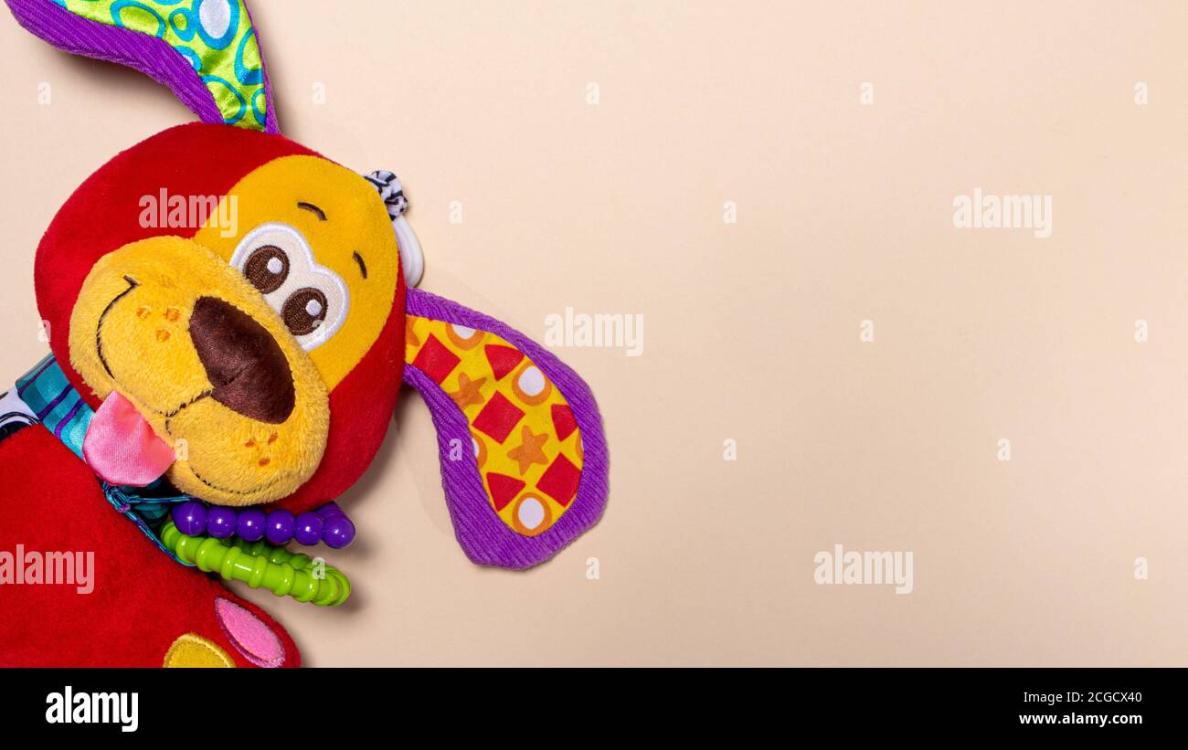 Red orange doggy toy on a beige background with room for text. Soft toy for baby dog banner for toy store. Stock Photo